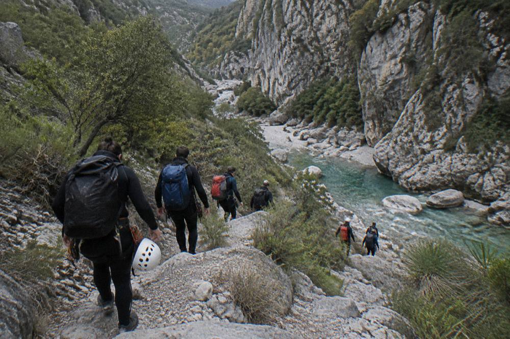 Canyoneers in wetsuits walking along a rocky canyon floor beside a stream