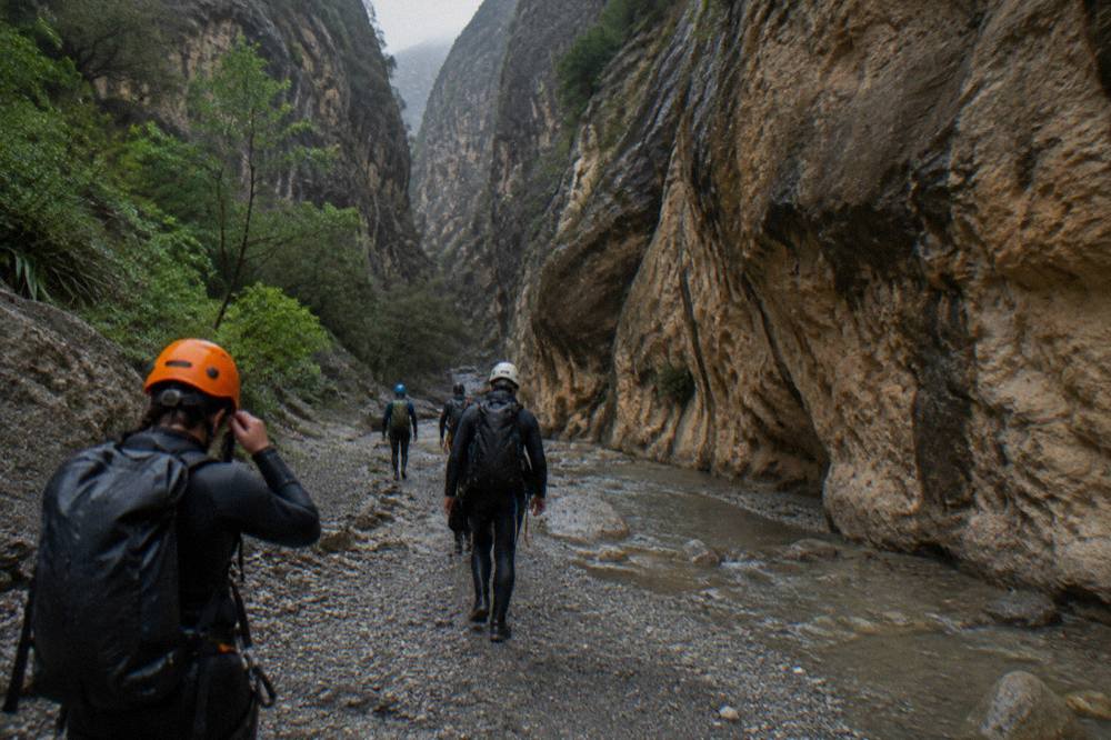 A wetsuit-clad group walking a canyon floor between tall rock walls