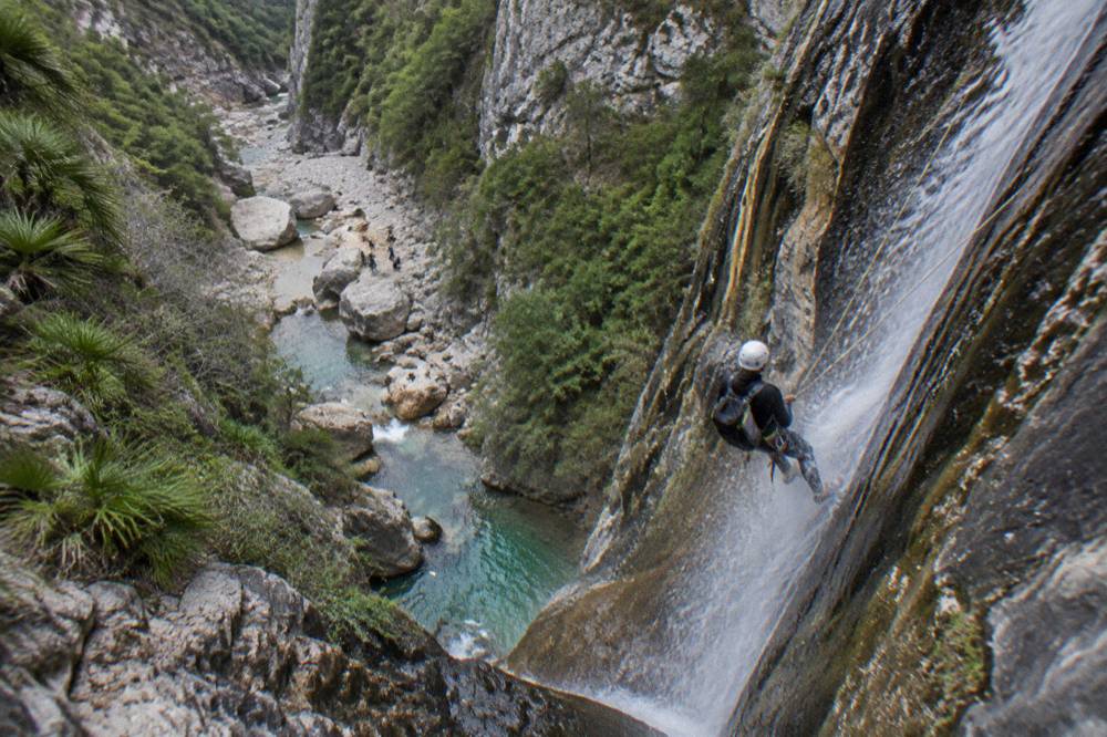 A canyoner on rappel descending a wet rock face beside falling water