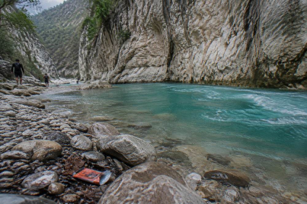Turquoise water swirling in a deep rock pool at the base of a canyon wall