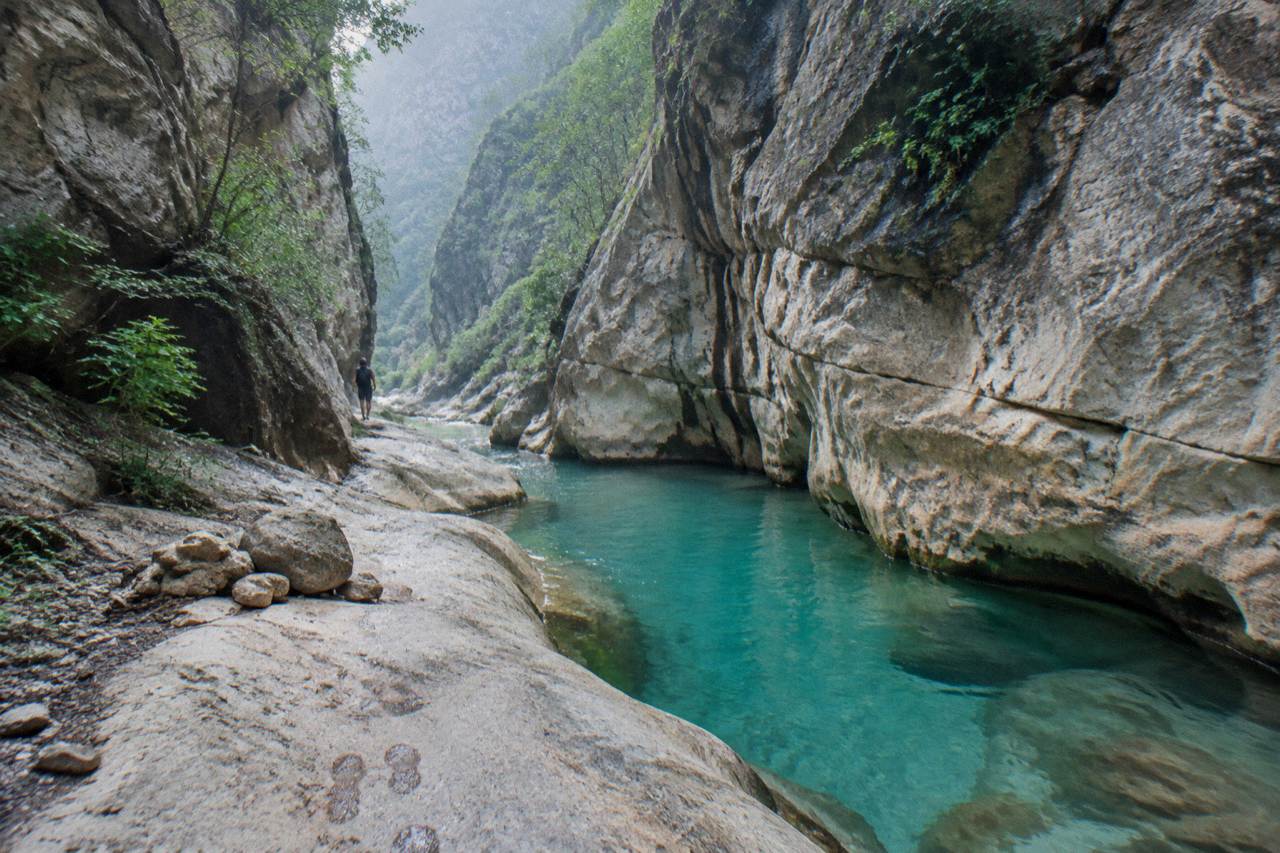 A narrow limestone canyon with turquoise water pooling between smooth rock walls