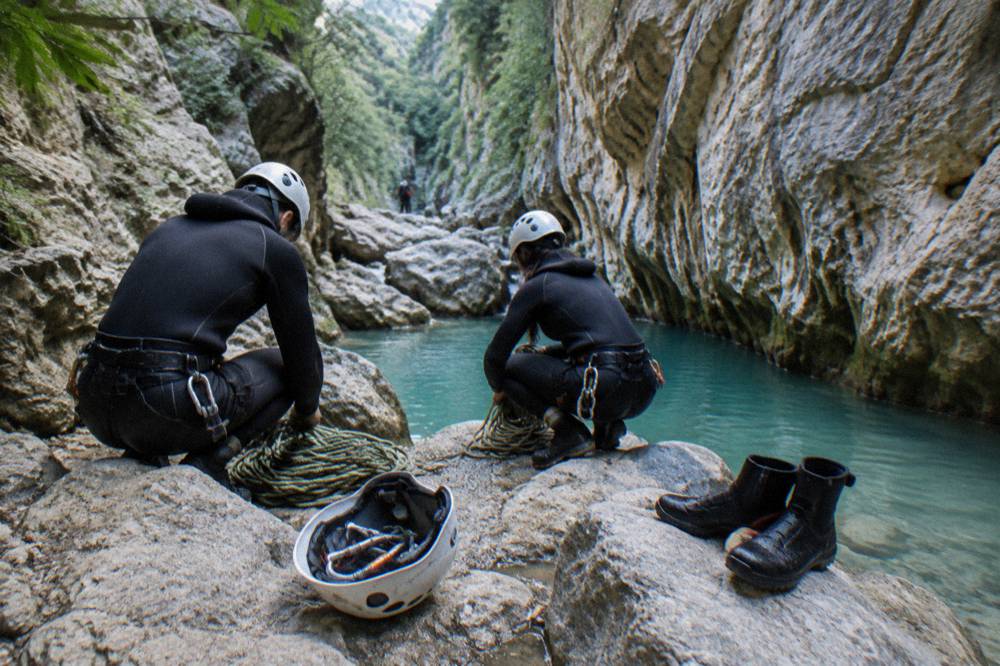 Canyoneers in wetsuits and helmets preparing ropes beside a turquoise pool in a narrow canyon