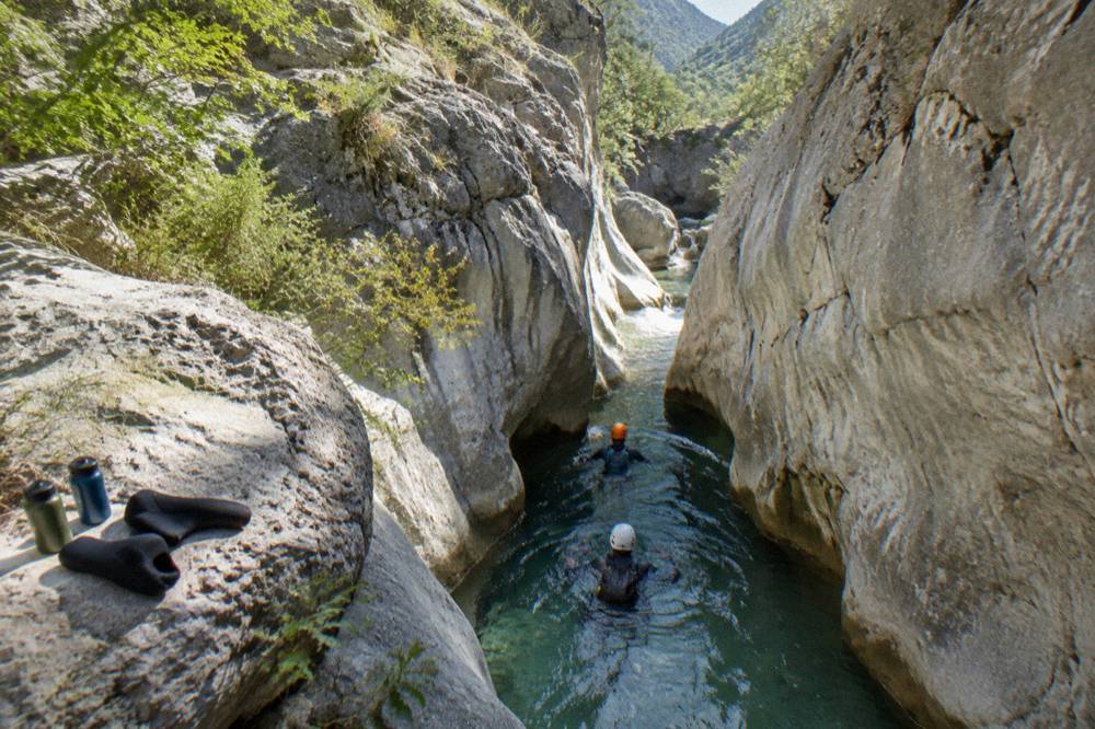 Canyoners swimming through a narrow water-filled passage between tall canyon walls