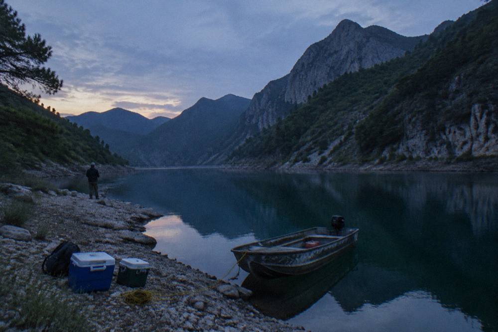 Lake shoreline at dusk with forested hills behind calm water