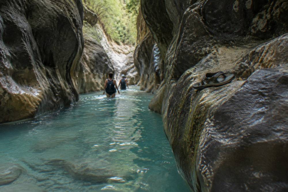 Narrow canyon passage with clear turquoise water between dark rock walls