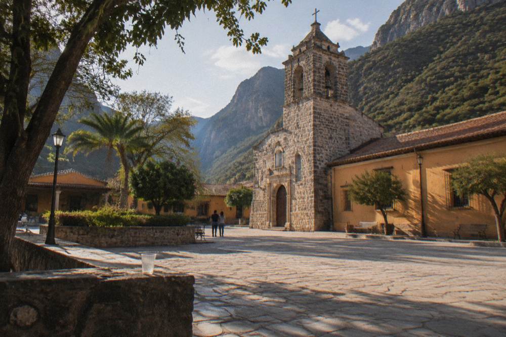Small-town plaza with a stone church and colorful facades under afternoon light