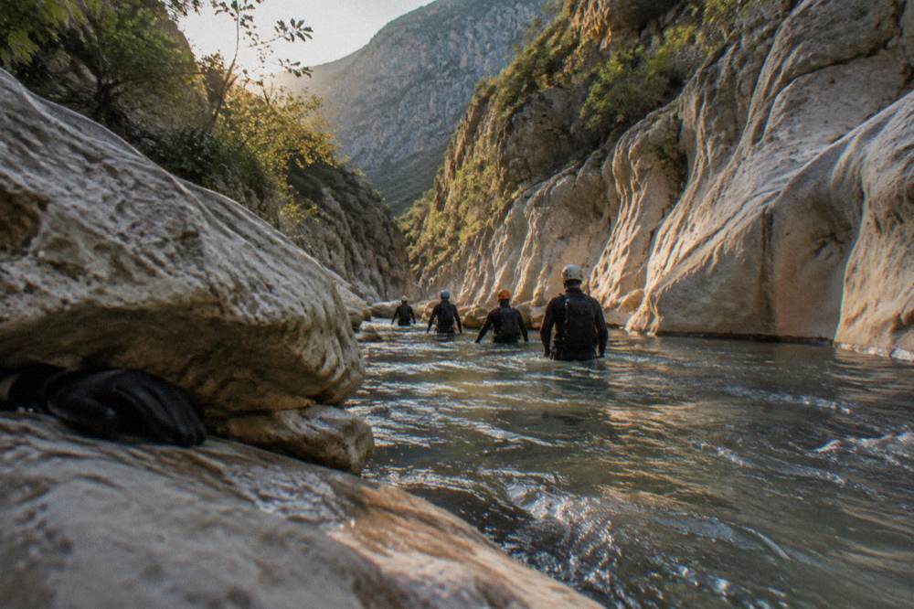 A group in wetsuits and helmets walking through a narrow canyon passage with flowing water
