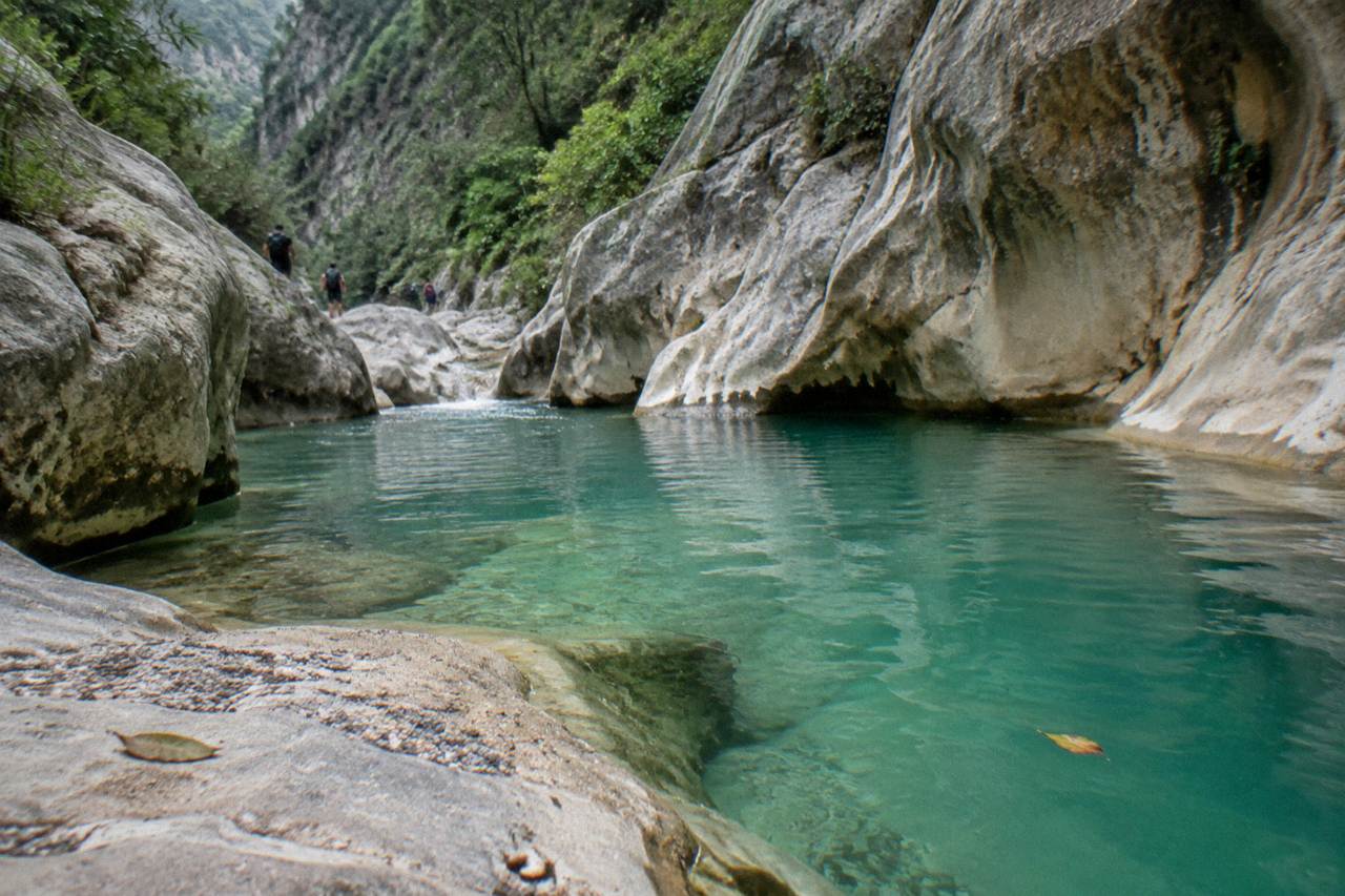A narrow limestone canyon with turquoise water pooling between smooth rock walls