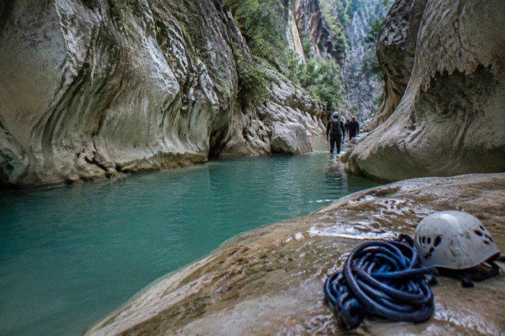 Turquoise water pooled between smooth rock walls inside a shaded canyon narrows