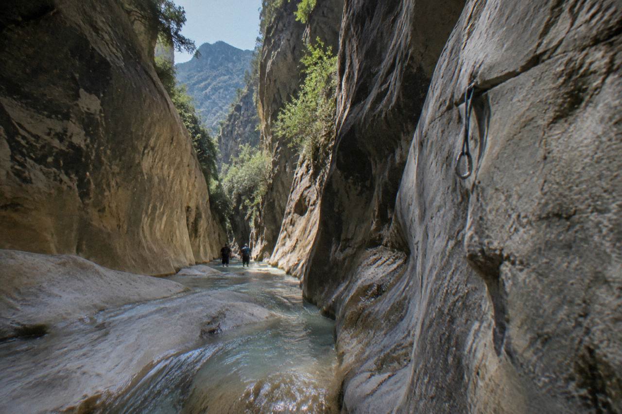 A narrow canyon passage with clear water flowing between tall rock walls