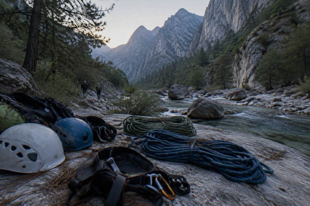 Canyoning helmets, harnesses and coiled ropes laid out on rock beside a river
