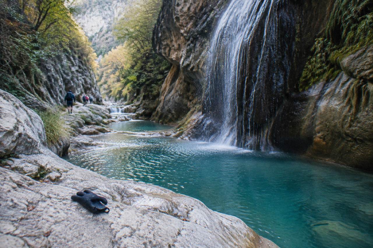 A narrow limestone canyon with turquoise pools and waterfall walls under morning light