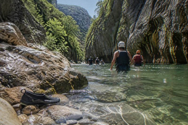 Canyoners in helmets and life jackets wading a green pool in Matacanes canyon