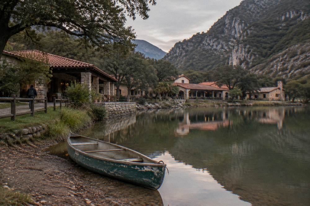 A calm lake surrounded by forested hills with small buildings on the shore
