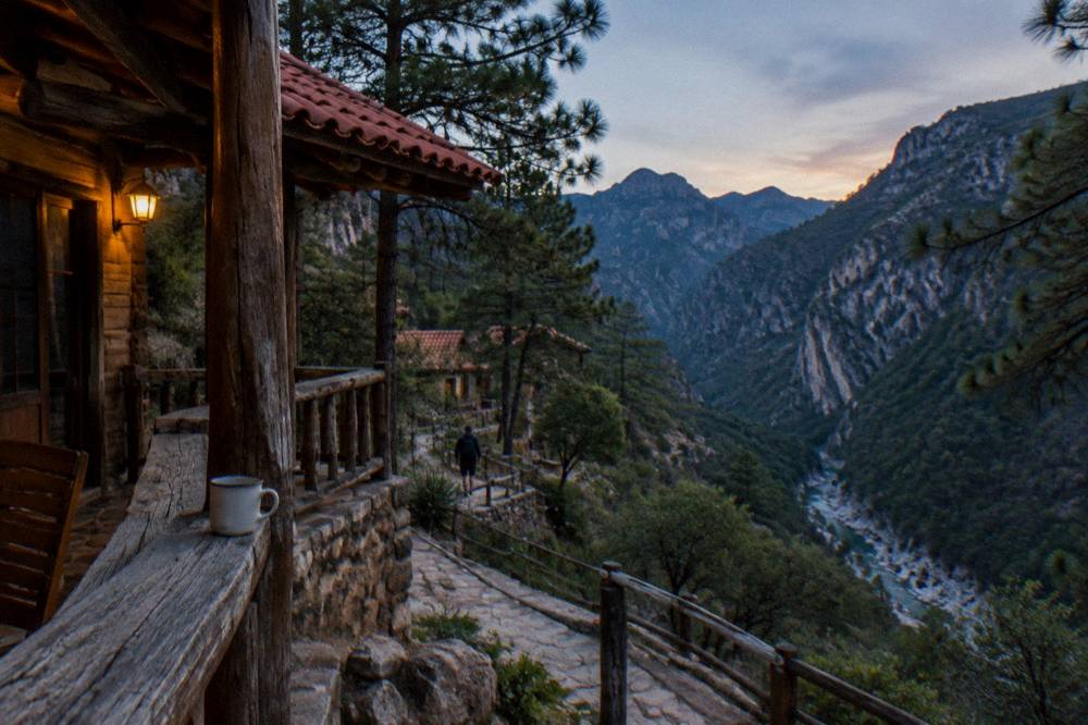 A wooden cabin with a porch among pine trees on a hillside