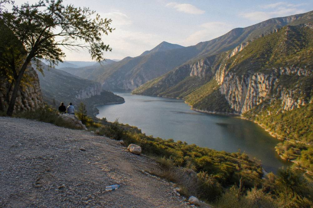 Wide mountain lake ringed by forested ridges under an afternoon sky