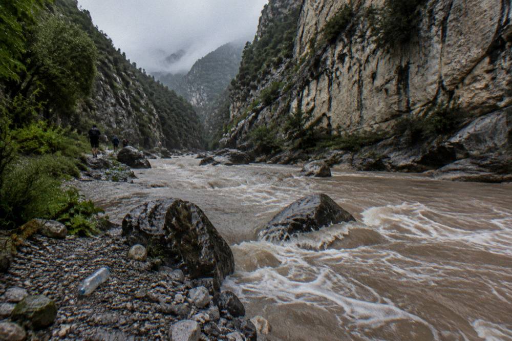 Swollen mountain river carrying brown water between rock walls after rain