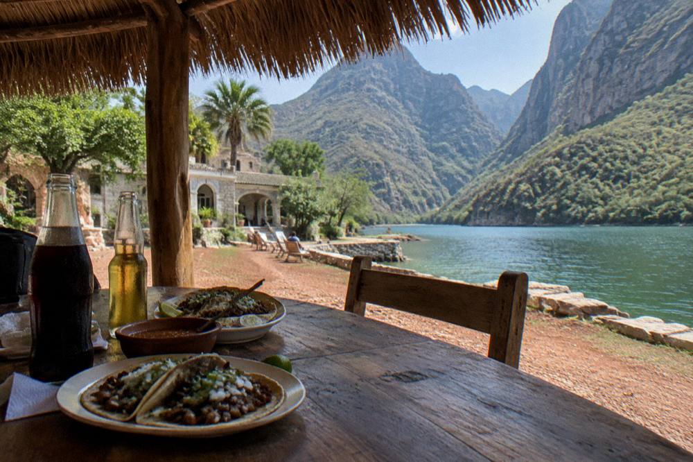 Tacos and cold drinks on a wooden table beside a lakefront road