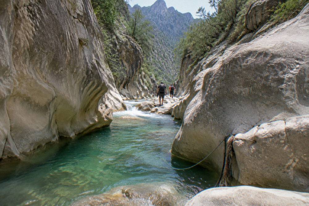 Deep narrow slot canyon with clear water flowing between smooth rock walls