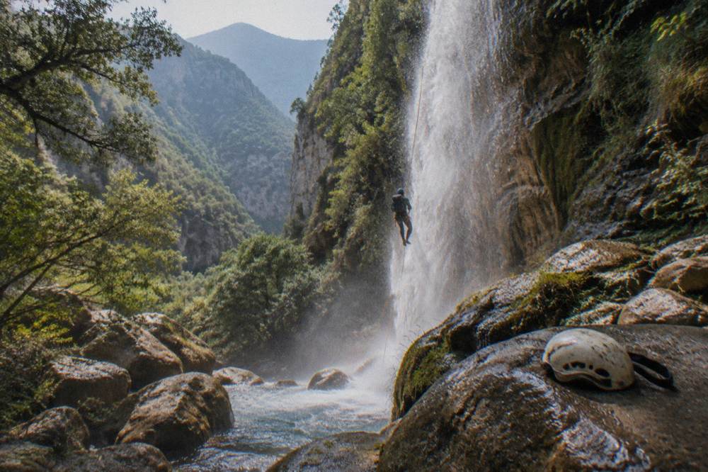 Canyoneer on a rope rappelling beside a tall waterfall in a green canyon