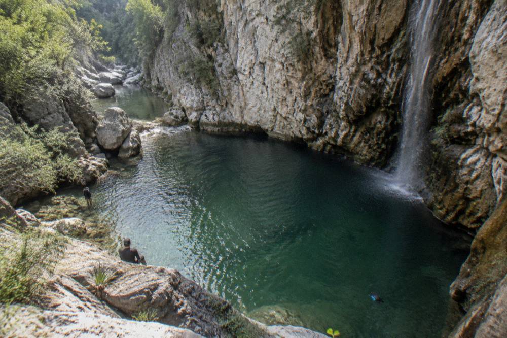 Deep green plunge pool at the base of a rock wall where a waterfall enters the canyon