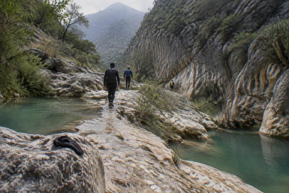 Hikers in wetsuits walking a rocky canyon trail between water sections