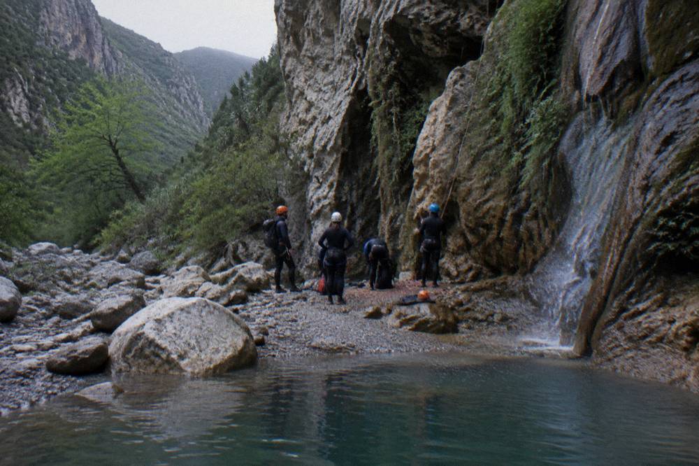Guided group in helmets and wetsuits gathered at the base of a canyon rappel