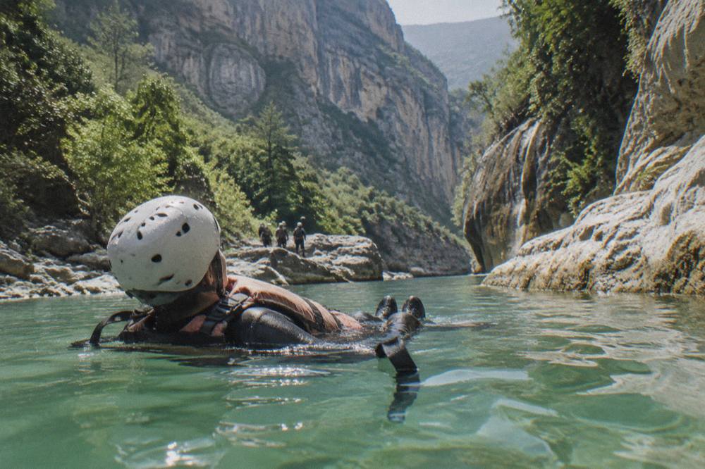 Canyoneer in helmet and life jacket floating in a green canyon pool