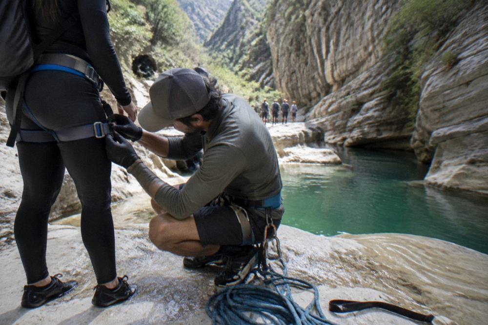 Guide checking a harness buckle beside a canyon pool