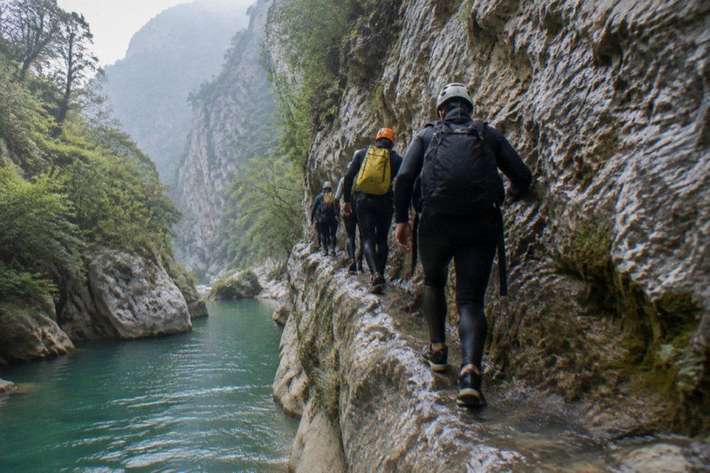 Line of canyoneers in wetsuits and helmets walking along a canyon ledge