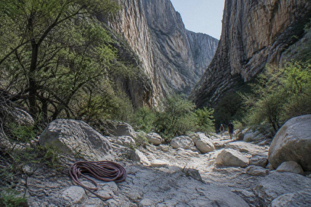 Tall limestone cliff walls of La Huasteca canyon above a dry rocky riverbed with scrub vegetation