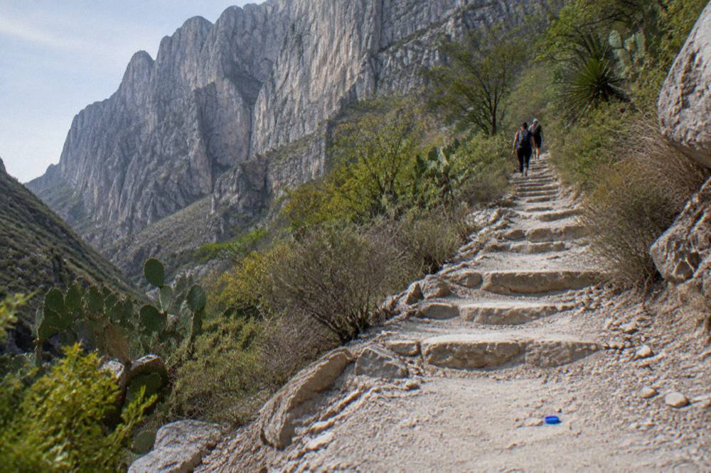 A steep hiking trail switchbacking up a dry hillside toward tall canyon cliffs