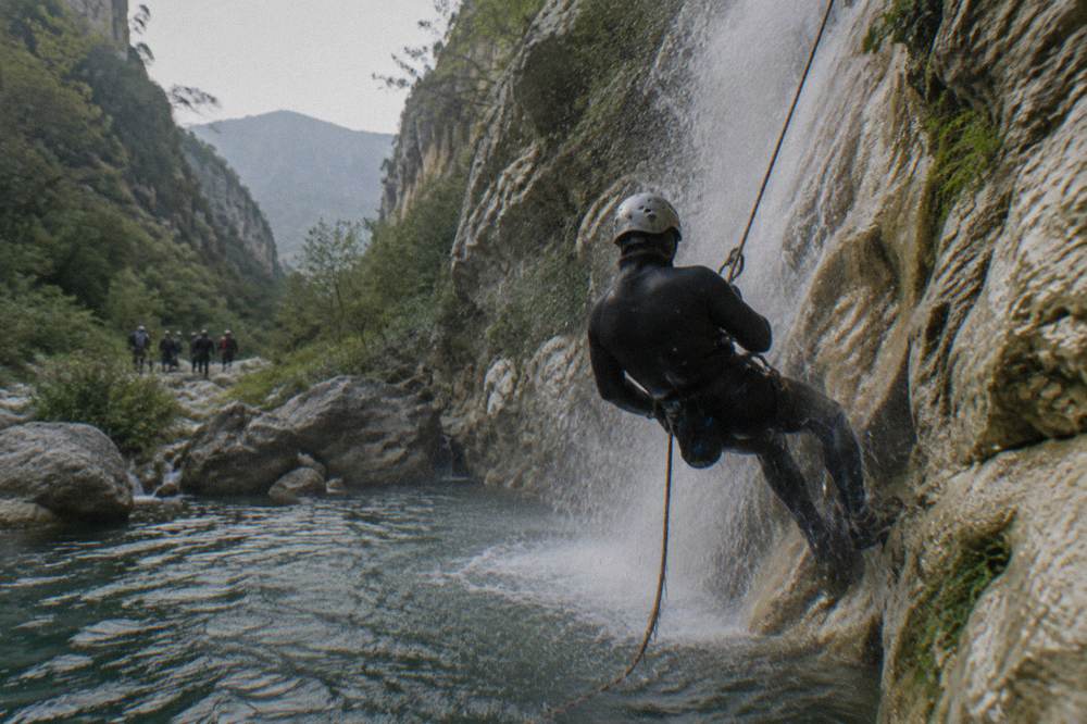 A canyoner in a wetsuit and helmet rappelling beside a waterfall into a dark pool
