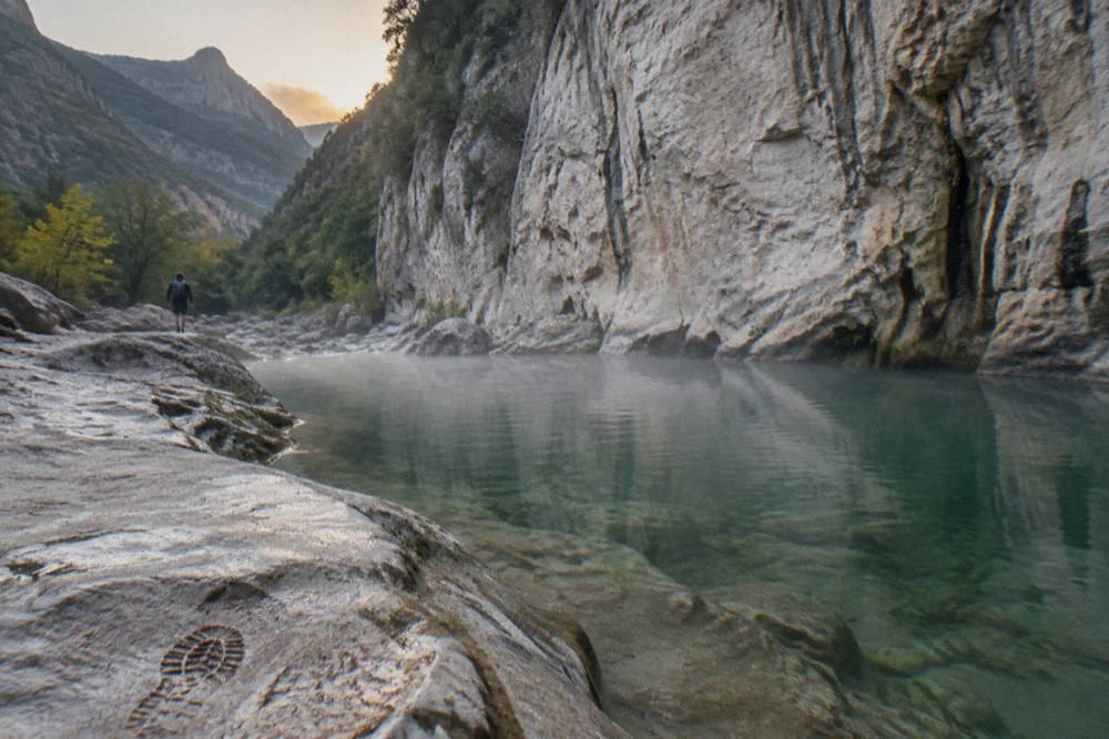 A calm pool of clear green water at the base of a canyon wall