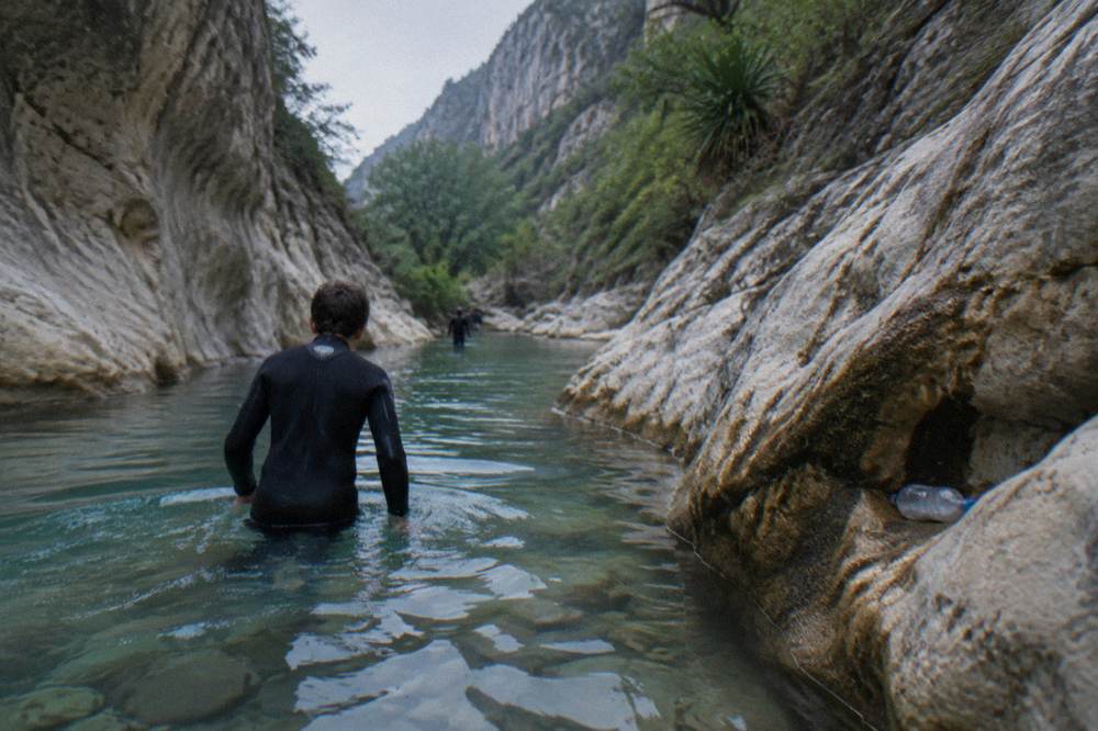 A canyoner in a wetsuit and helmet wading through a narrow water channel