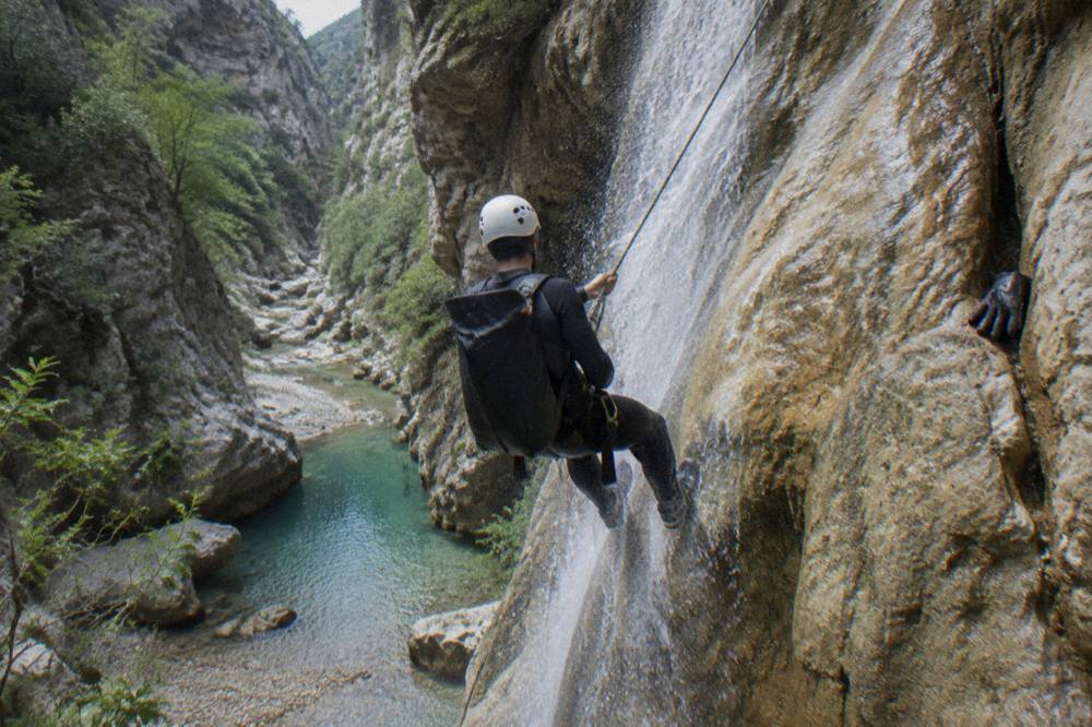 Canyoneer on a rope rappelling down a wet rock wall beside a narrow waterfall