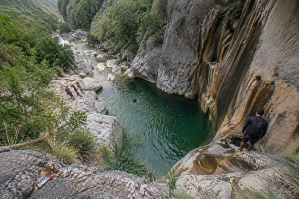 Deep green pool at the base of a rock wall where canyon jumps land