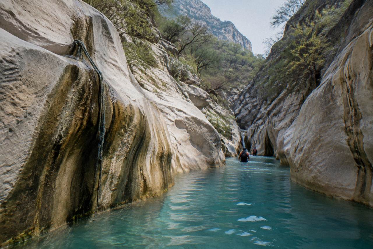 Narrow limestone canyon with turquoise water pooling between smooth rock walls