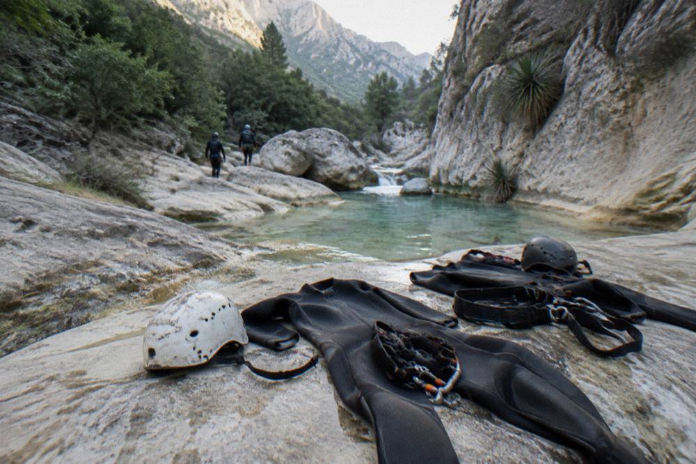 Neoprene wetsuits helmets and harnesses laid out on rocks