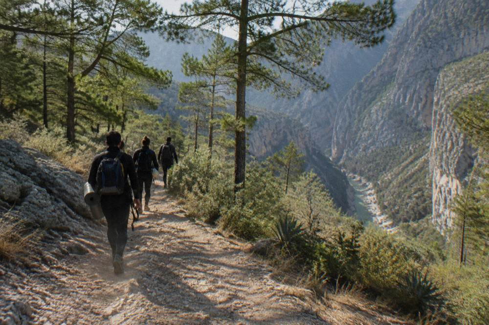 Hikers in wetsuits walking a dirt trail toward a canyon rim