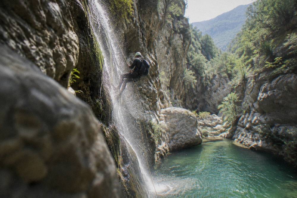 Canyoneer on rope rappelling beside a waterfall into a pool