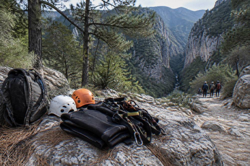 A row of canyoning helmets, harnesses and folded wetsuits laid out on a rock before a descent