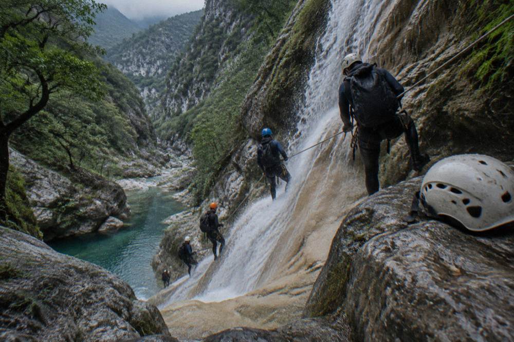 A line of guided canyoneers clipped to a rope during a waterfall descent inside a canyon
