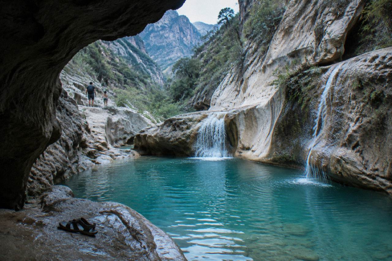 A turquoise pool inside a narrow limestone canyon with waterfalls feeding into it