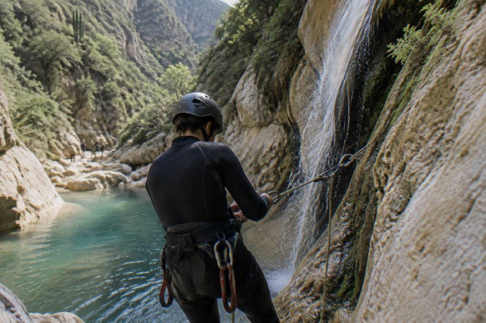 Canyoneer in a wetsuit preparing to rappel beside a waterfall
