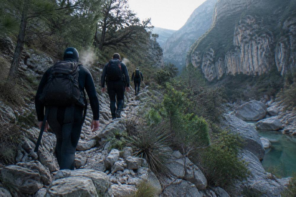 Group of hikers in wetsuits walking a canyon trail in morning light