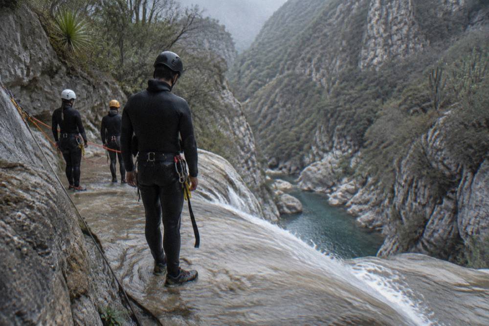 A small group of canyoneers rigged on ropes at the top of a waterfall rappel