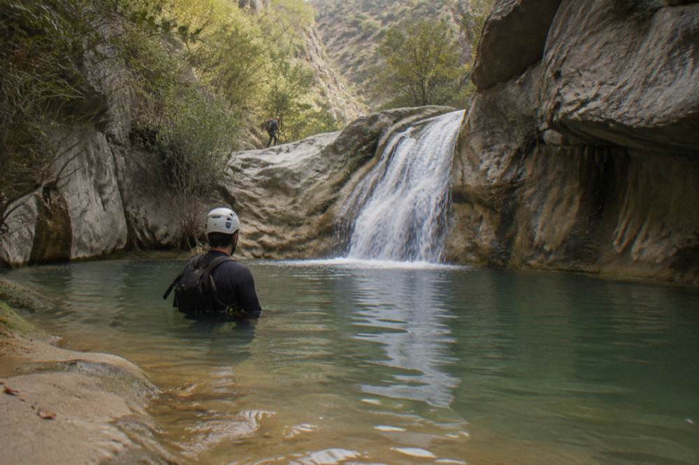 A canyon pool at the base of a waterfall with a guide waiting in an eddy