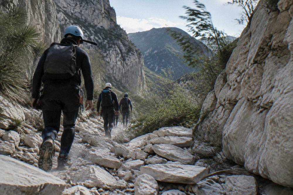 Canyoneers in wetsuits walking a rocky trail between canyon walls