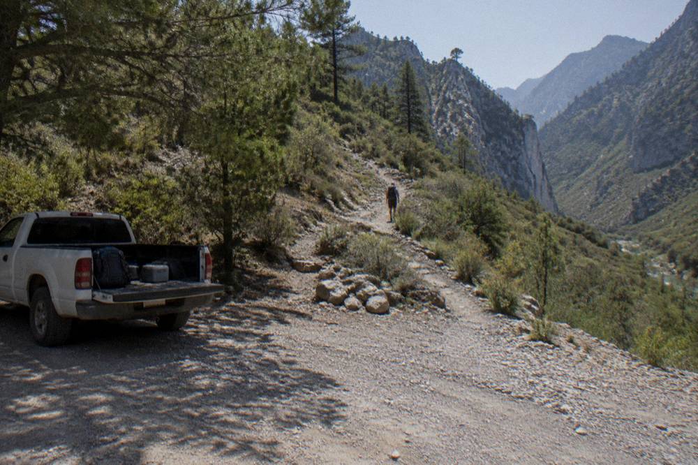 Steep dirt mountain road winding toward a canyon trailhead